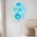 Azure Bloom designer crystal wall lighting with radiant blue floral glass and gold accents, mounted above a bed in a luxury bedroom setting.