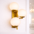 Luxury gold wall sconce with three frosted globe lights, ideal for modern elegant interiors. Features warm LED lighting and premium brass finish.