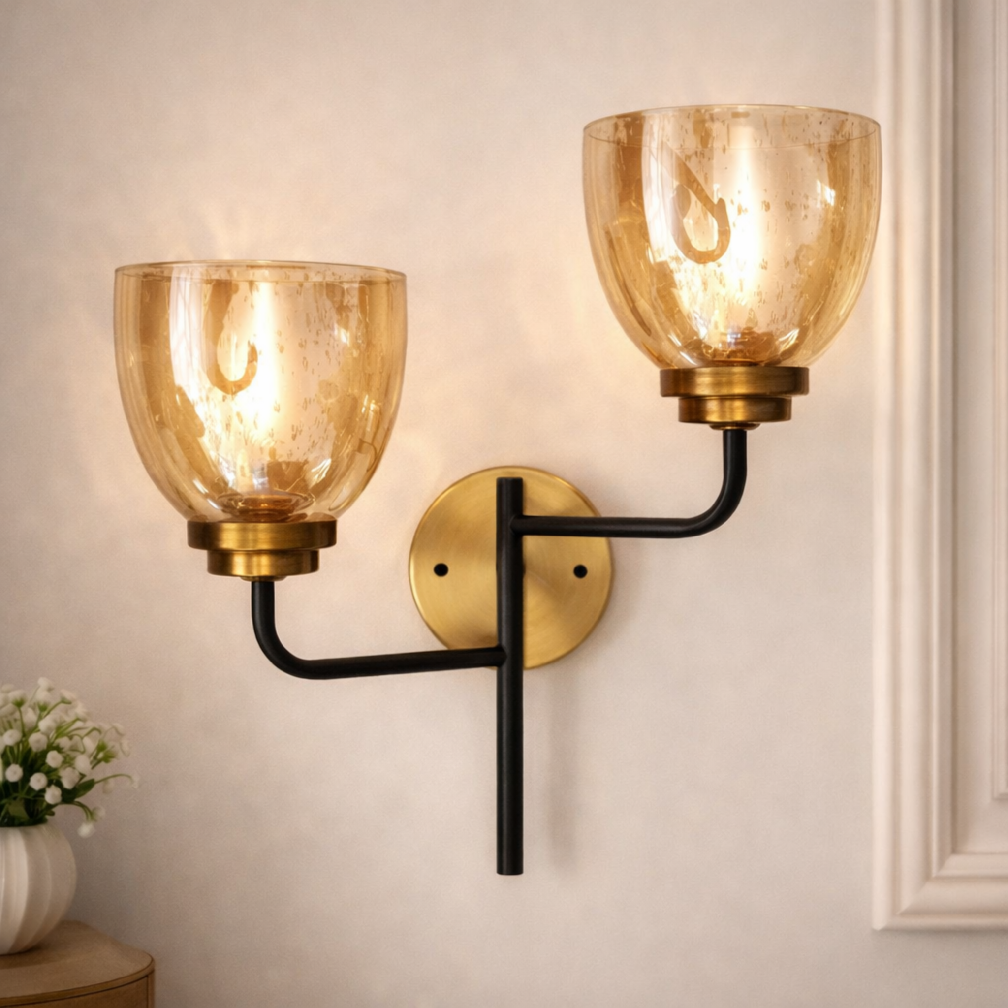 DuoAura dual arm glass wall sconce with amber glass shades, brass accents, and black metal arms mounted on a beige wall. Ideal for luxury home lighting.